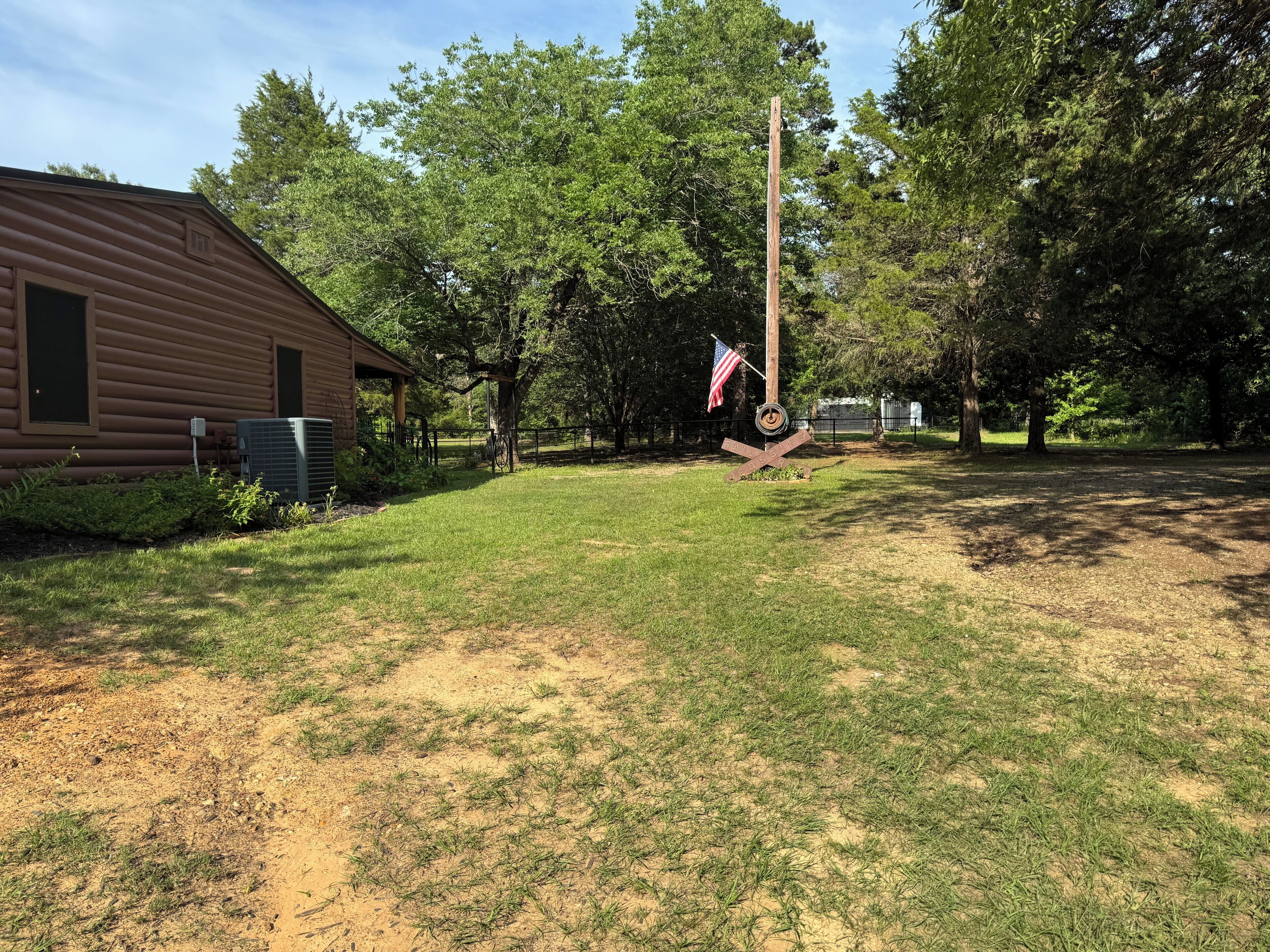 A wooden cabin with a grassy yard, a flagpole with an American flag, and a fence.