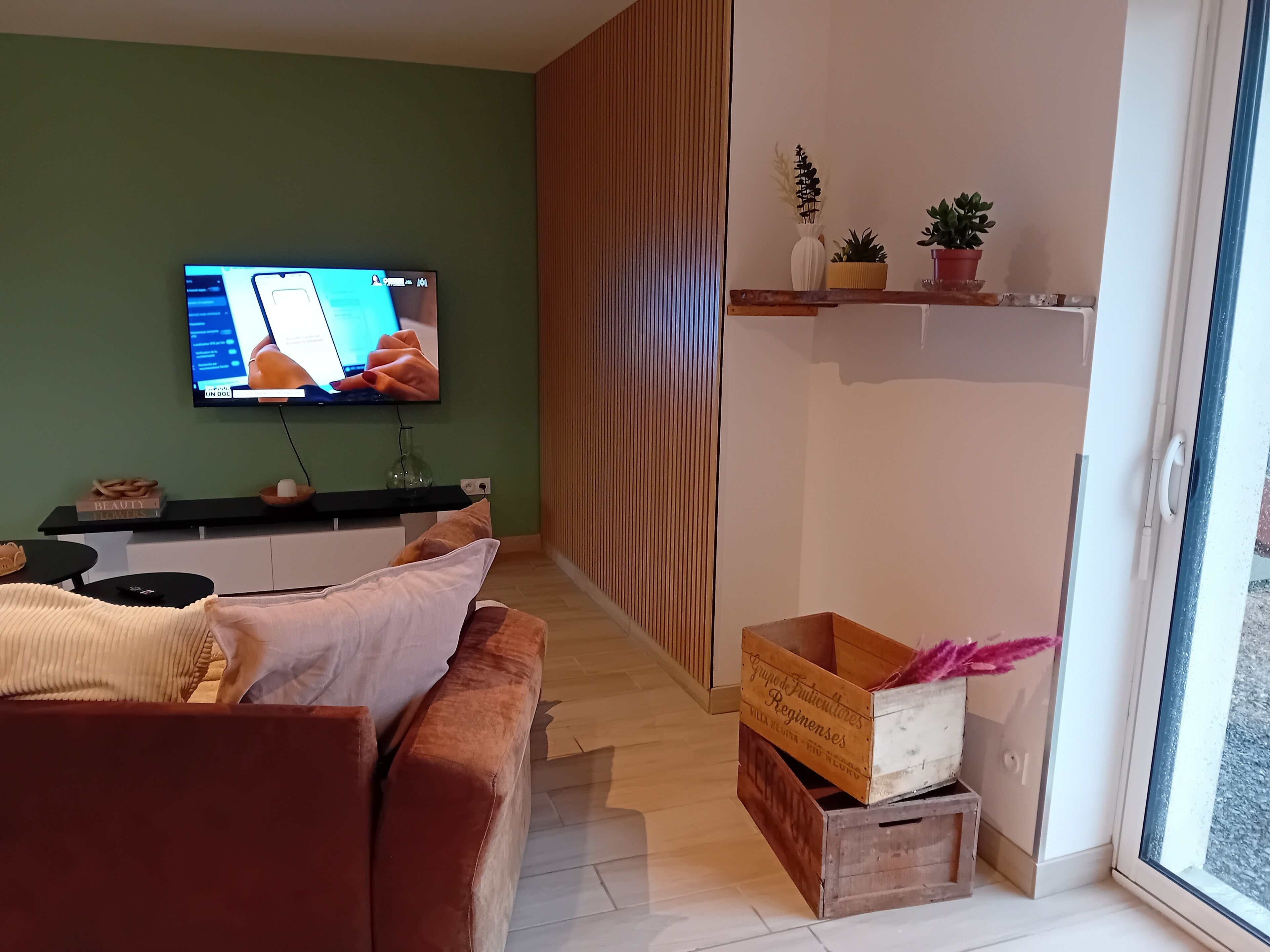 Una sala de estar con televisor, sofá, separador de madera y ventana.