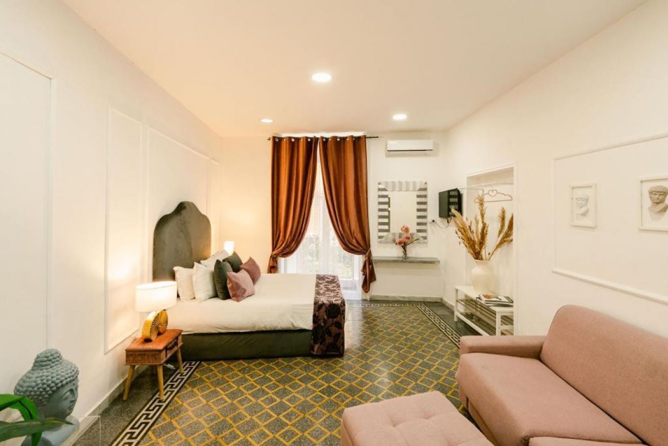 Une chambre d’hôtel avec un lit, un canapé, une table de chevet et une petite table avec une lampe.