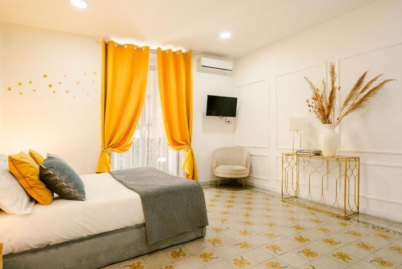 A hotel room with a bed, a chair, a TV, and a small table with a vase.