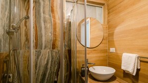 A bathroom with a glass-enclosed shower, a wooden vanity with a sink, and a round mirror. - Random Apartment Deluxe (Naples)