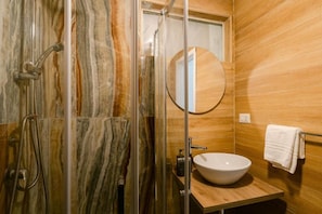A bathroom with a glass-enclosed shower, a wooden vanity with a sink, and a round mirror. - Random Apartment Deluxe (Naples)