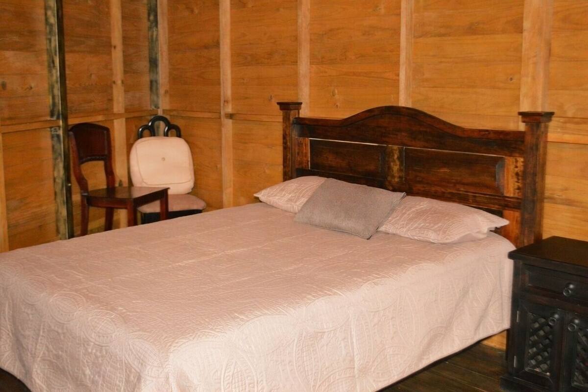 A wooden-paneled room with a bed, a chair, and a nightstand.