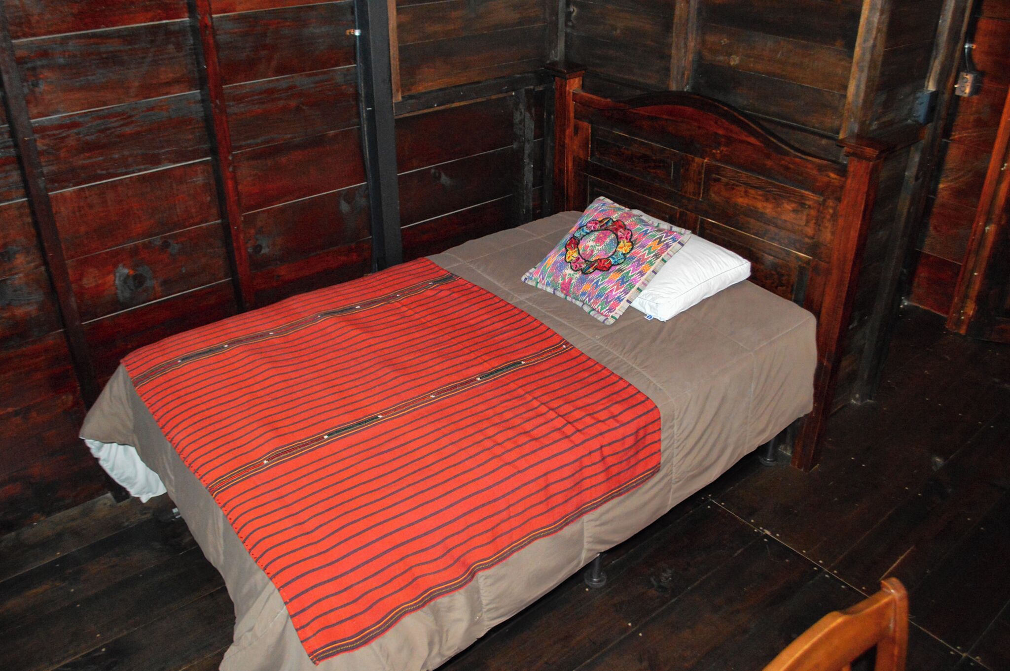 A single bed with a red-striped bedspread and a white pillow in a room with wooden walls and a wooden headboard.