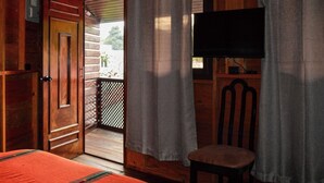 A wooden cabin room with a bed, a chair, a TV, and a door leading to a balcony. - El Refugio - Hospedaje y Eventos (San Lucas Sacatepequez)