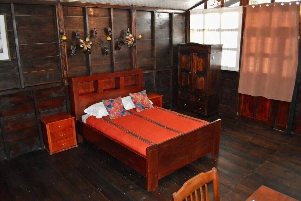 A wooden bed with a red bedspread, a wooden nightstand, a wooden wardrobe, and a wooden chair.