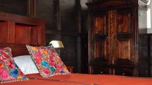 A bed with floral pillows, a wooden headboard, and a nightstand with a lamp. - El Refugio - Hospedaje y Eventos (San Lucas Sacatepequez)