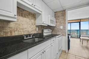Une cuisine avec des meubles blancs, un plan de travail noir, un four à micro-ondes et une cuisinière.