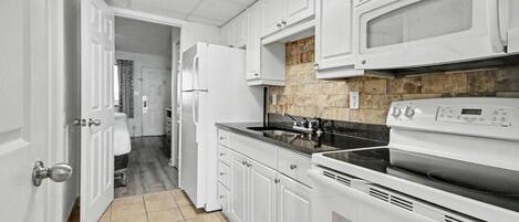 A kitchen with white cabinets, a microwave, a stove, and a tiled floor.