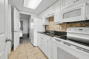 A kitchen with white cabinets, a microwave, a stove, and a tiled floor. - Oceanfront 1BR + Beach Access + Dog Friendly (Myrtle Beach)