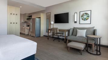 Et moderne hotelværelse med seng, sofa, skrivebord, stol, fjernsyn og et tekøkken.
