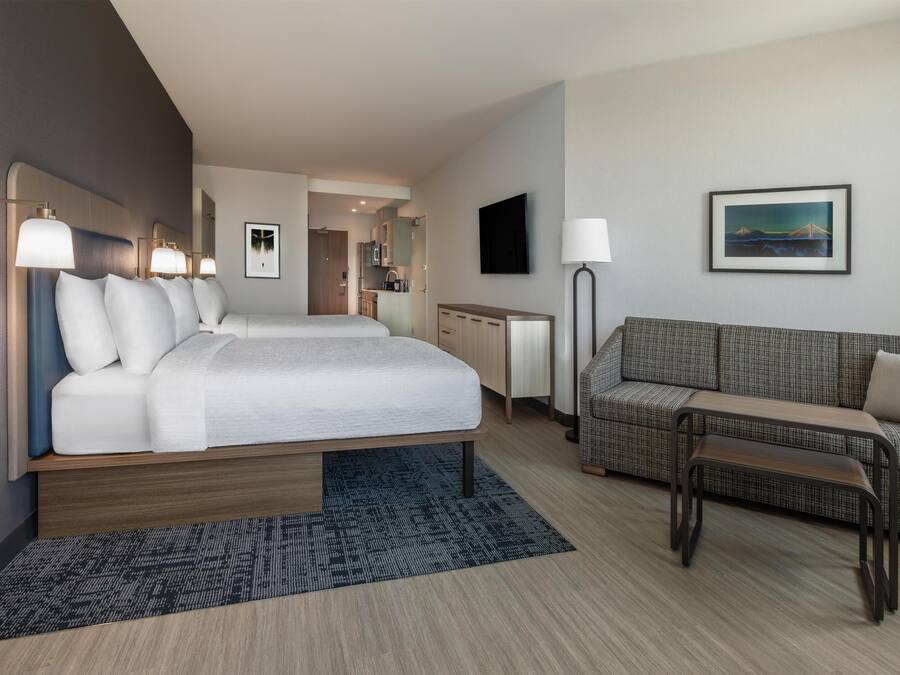 Quarto de hotel com cama, sofá, mesa de centro, televisão e um quadro na parede.