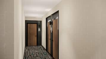 A hallway with patterned flooring, a wooden door, and a wall-mounted light fixture.