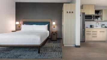 Una habitación de hotel con cama, lámparas de noche, una mesita auxiliar pequeña, una zona de cocina con microondas y un armario.