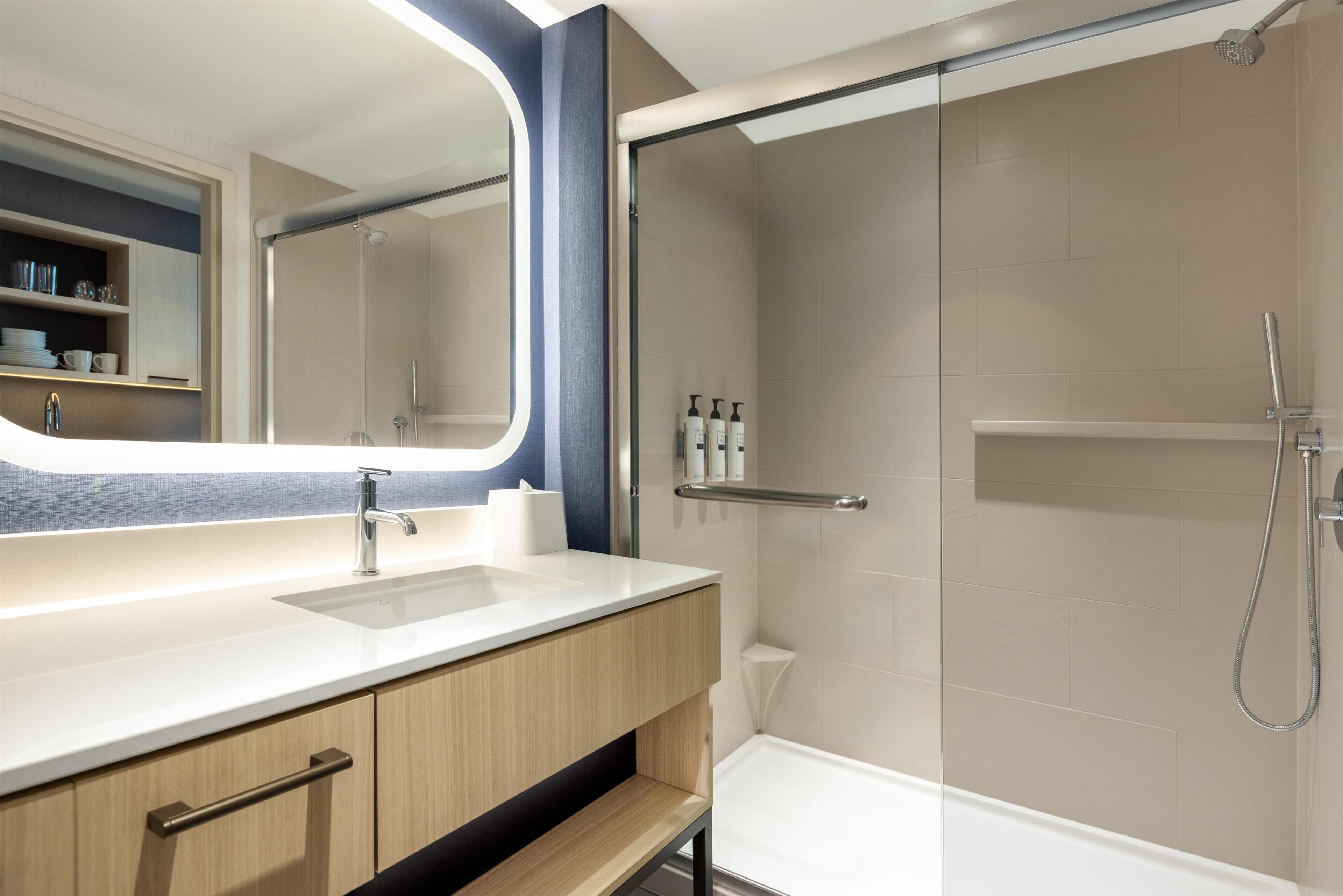 A modern bathroom with a sink, mirror, shower, and storage cabinets.