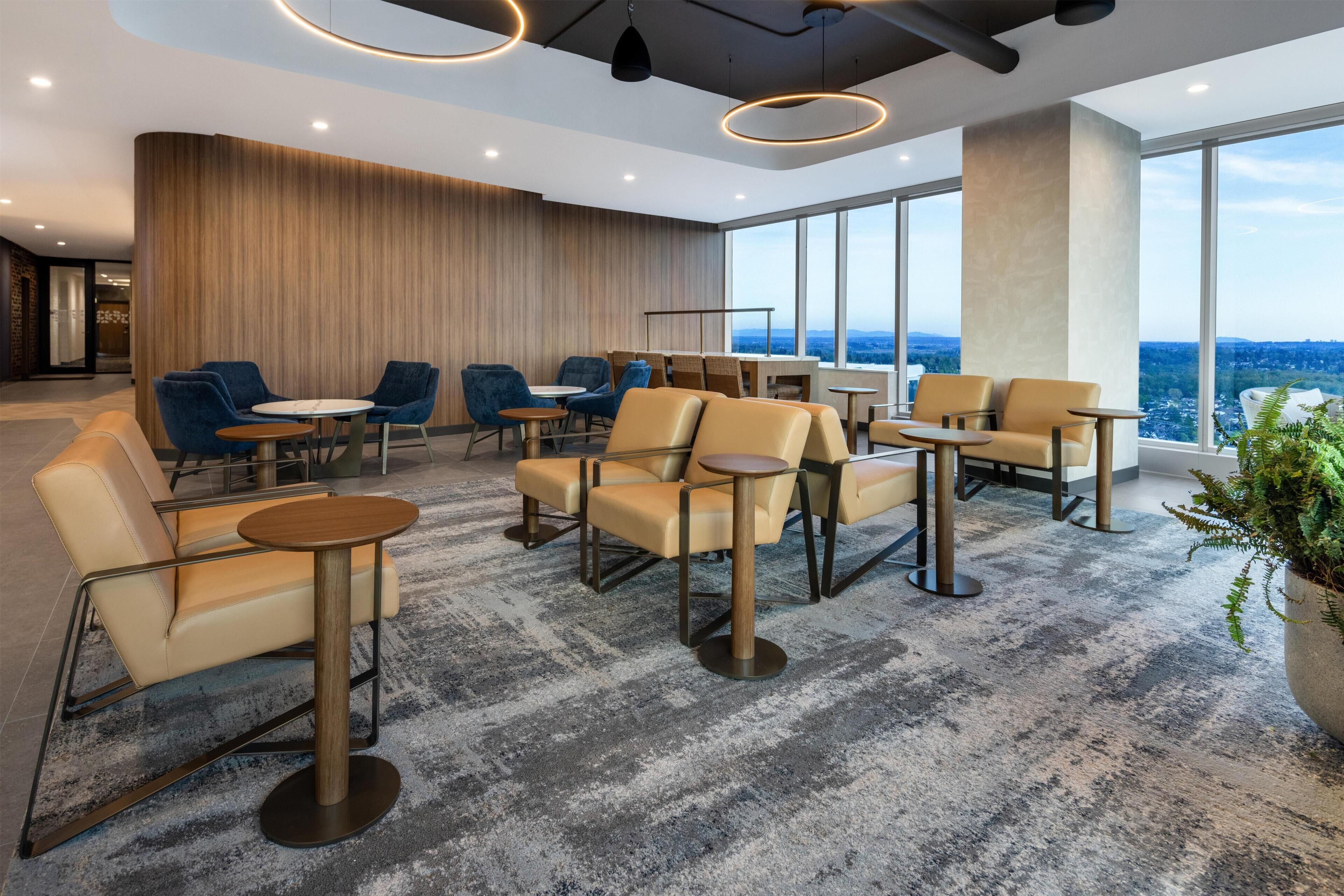 A modern lounge with leather chairs, round tables, and large windows offering a city view.