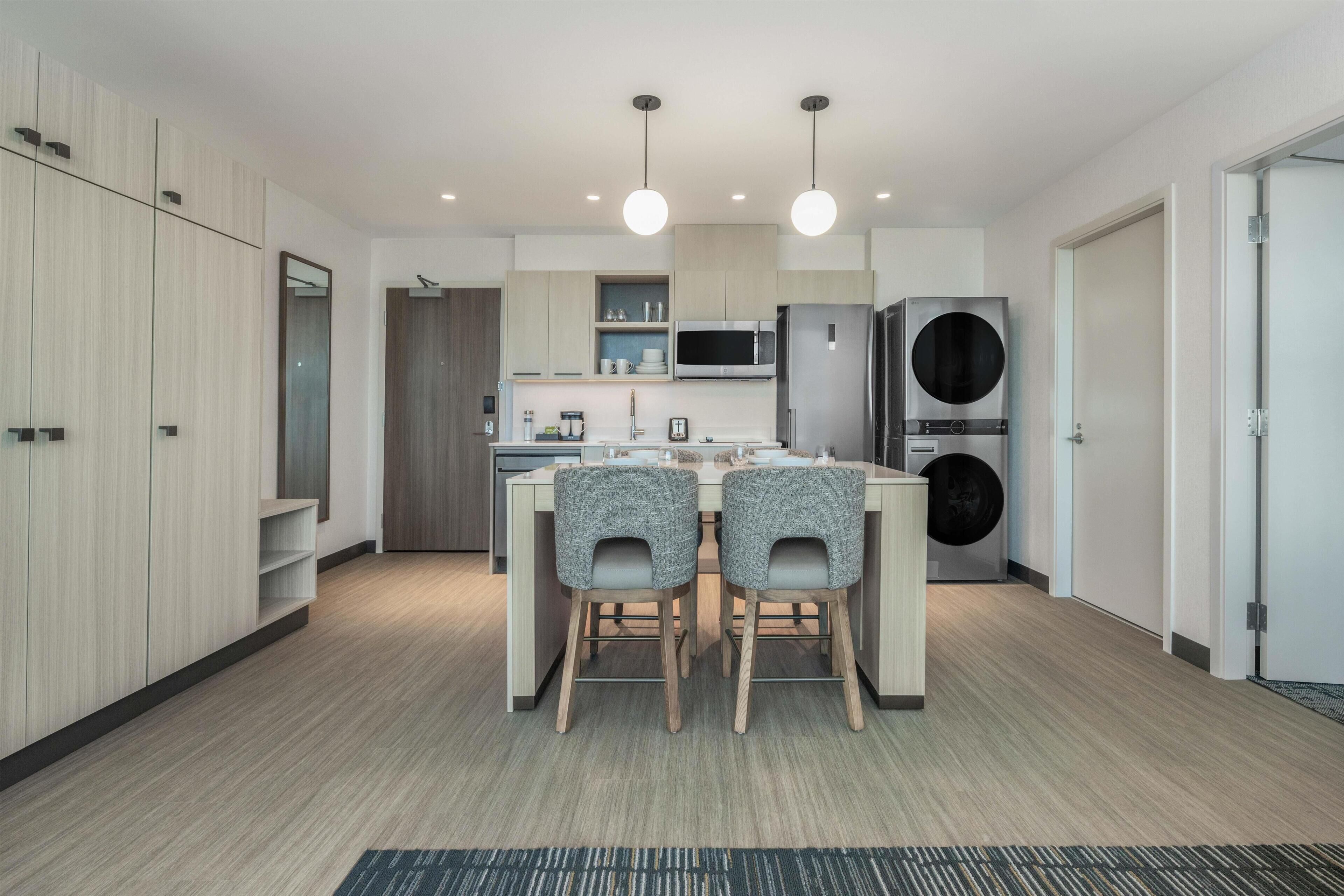 Cocina moderna con una isla central, dos sillas, microondas, refrigerador y lavadora.