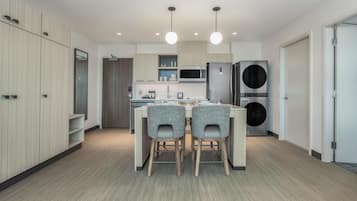 Cocina moderna con una isla central, dos sillas, microondas, refrigerador y lavadora.