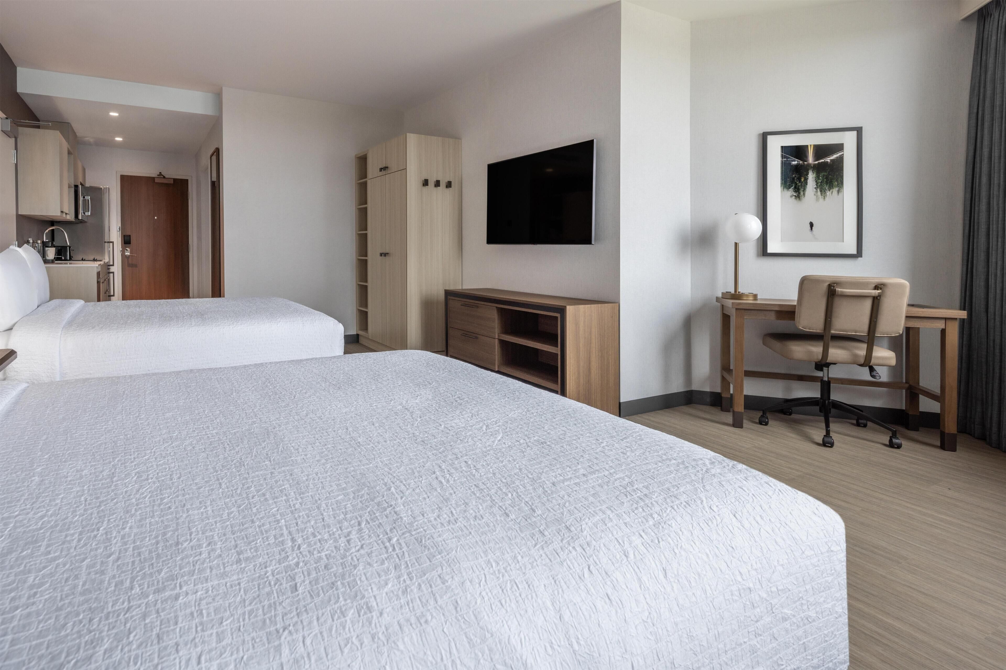 A hotel room with two beds, a desk, a chair, a TV, and a wardrobe.