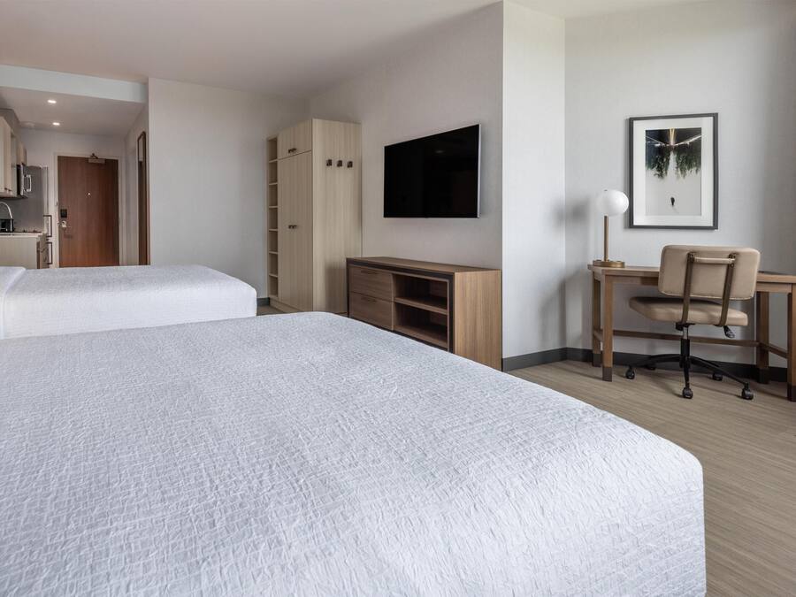 A hotel room with two beds, a desk, a chair, a TV, and a wardrobe.