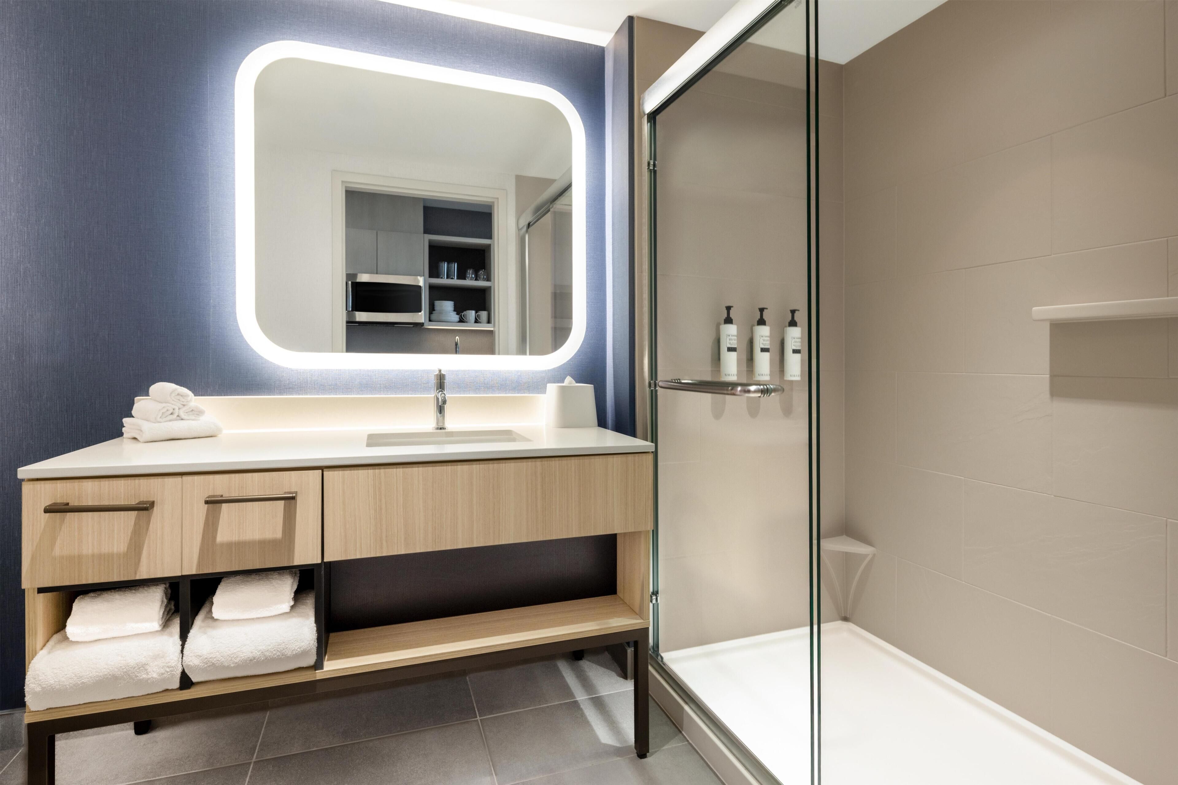 Un baño moderno con un espejo grande, un lavamanos, una ducha y un tocador con toallas.