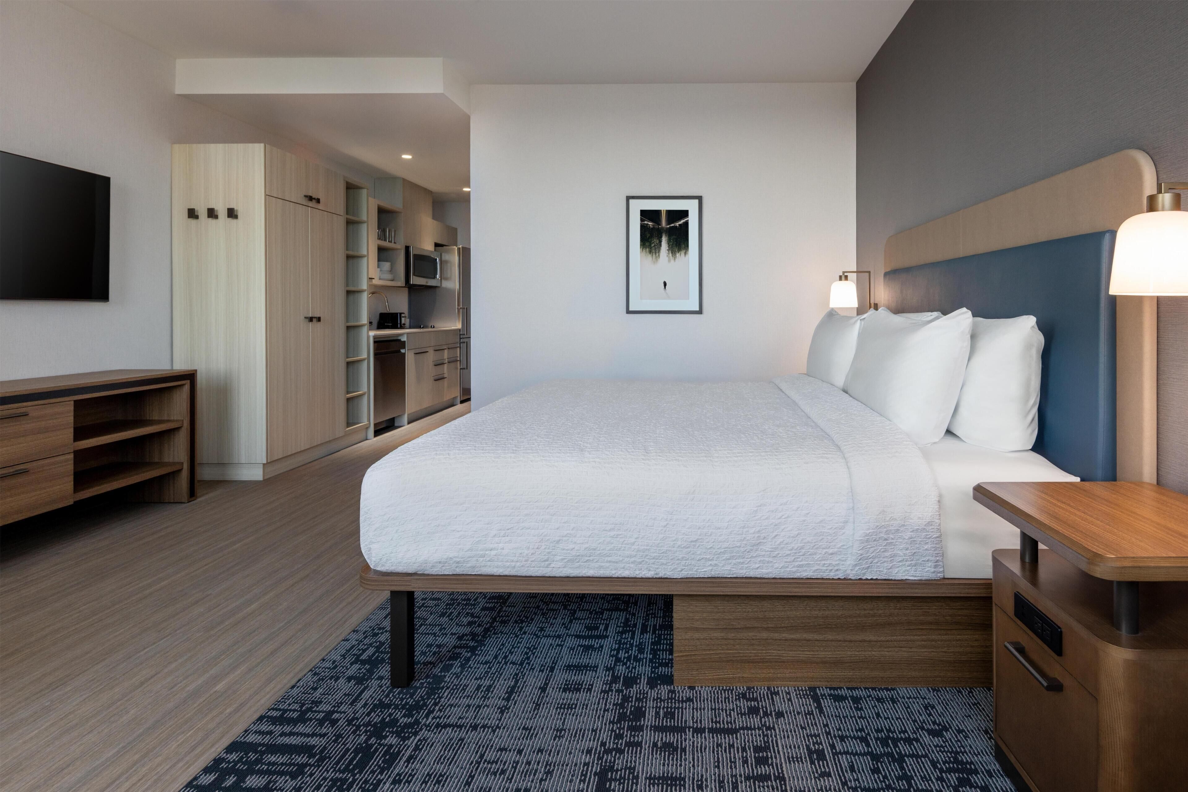 A modern hotel room with a large bed, a TV, a wardrobe, and a desk.
