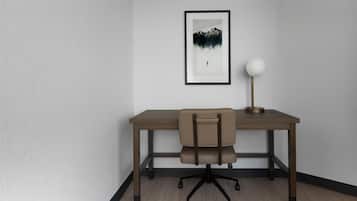 A room with a desk, chair, framed artwork, and a lamp.