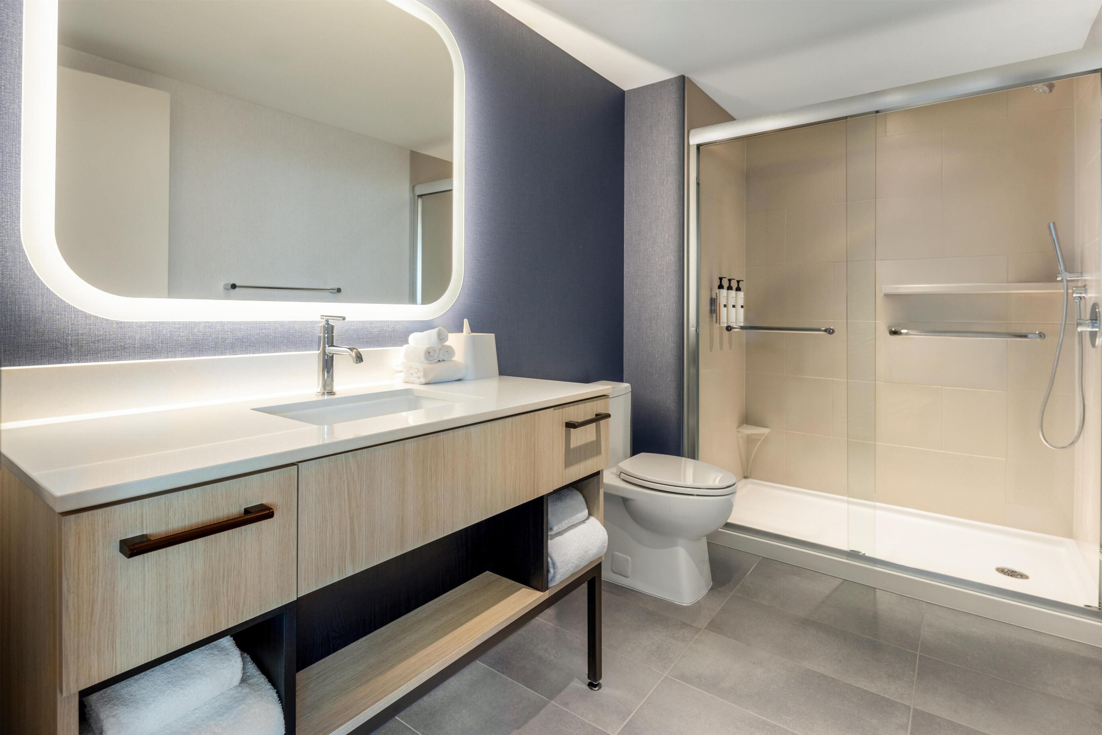 A modern bathroom with a large mirror, a sink, a toilet, and a glass-enclosed shower.