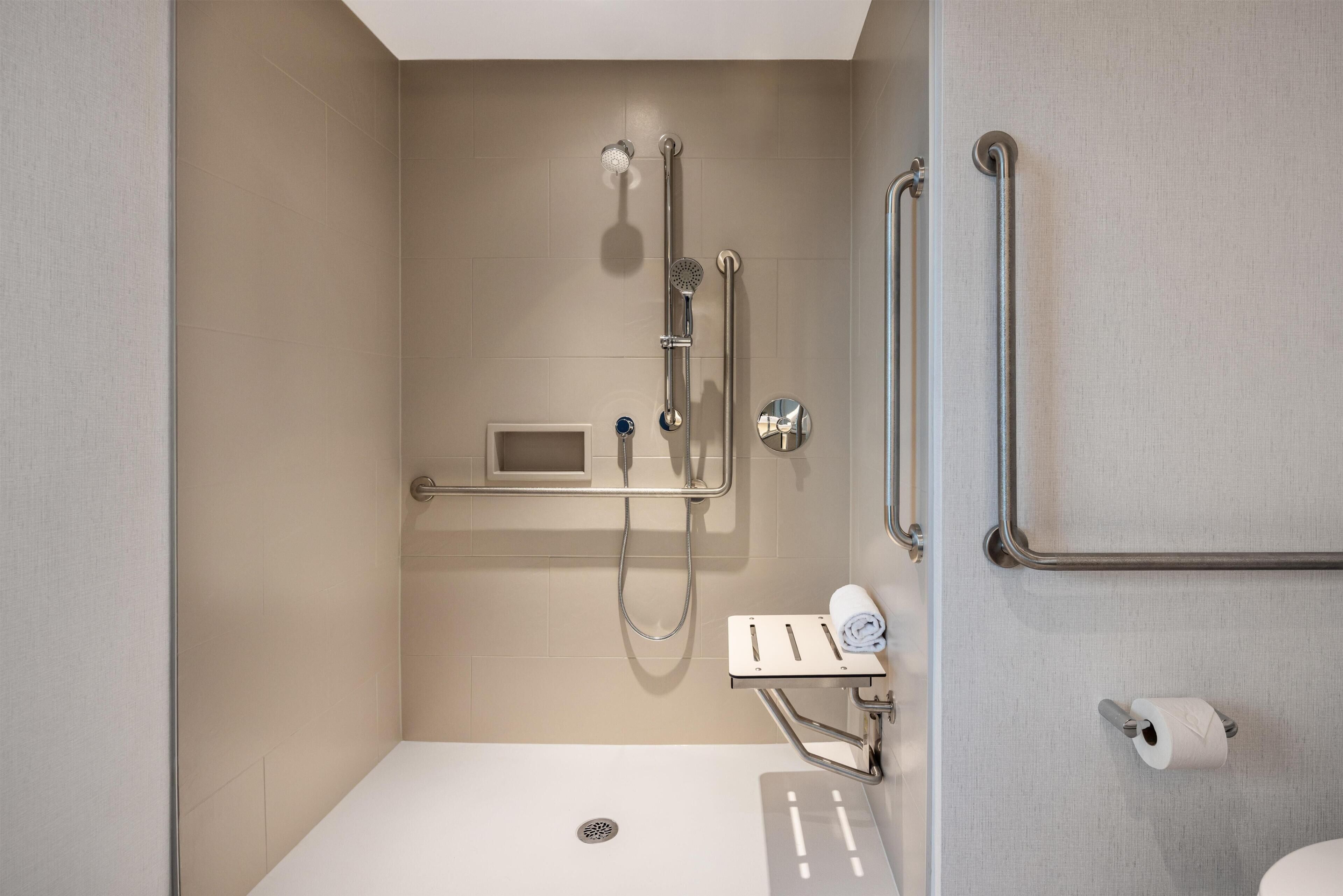 A modern bathroom with a shower, grab bars, a towel rack, and a toilet paper holder.