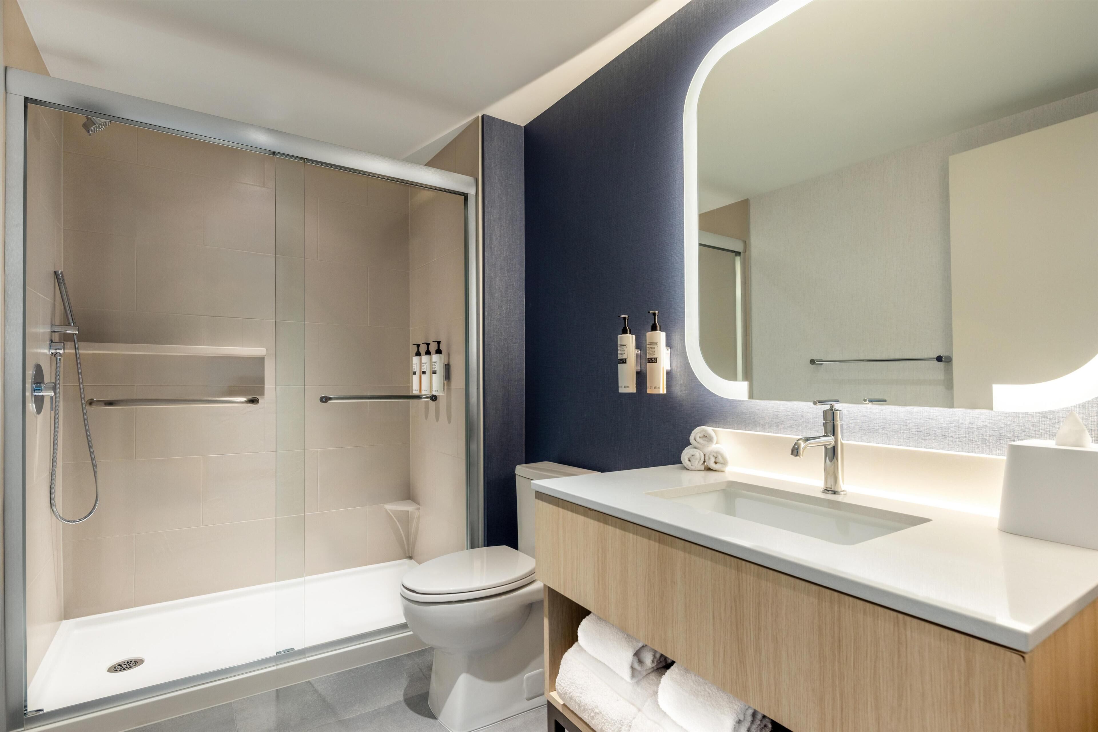 A modern bathroom with a glass-enclosed shower, a white toilet, a vanity with a mirror, and a sink.