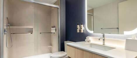 Un baño moderno con ducha envuelta en vidrio, inodoro blanco, tocador con espejo y lavamanos.