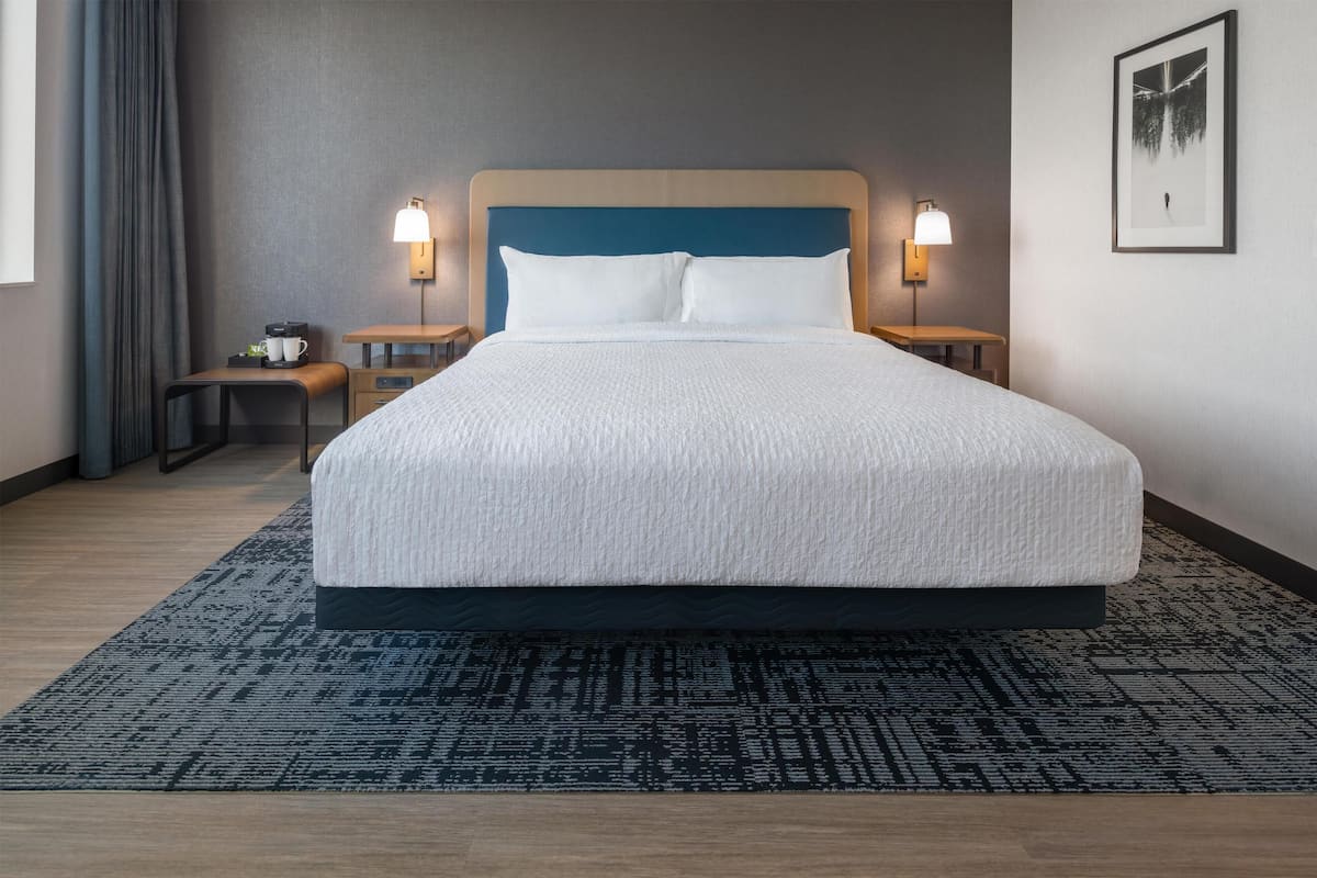 Hotellihuone, jossa on suuri sänky, yöpöydät, lamppu, seinällä oleva taulu ja ikkuna, jossa on verhot.