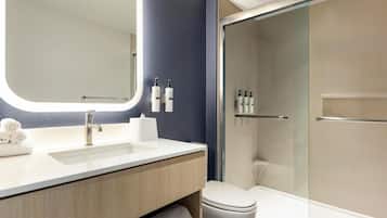 A modern bathroom with a sink, mirror, toilet, and glass shower enclosure.