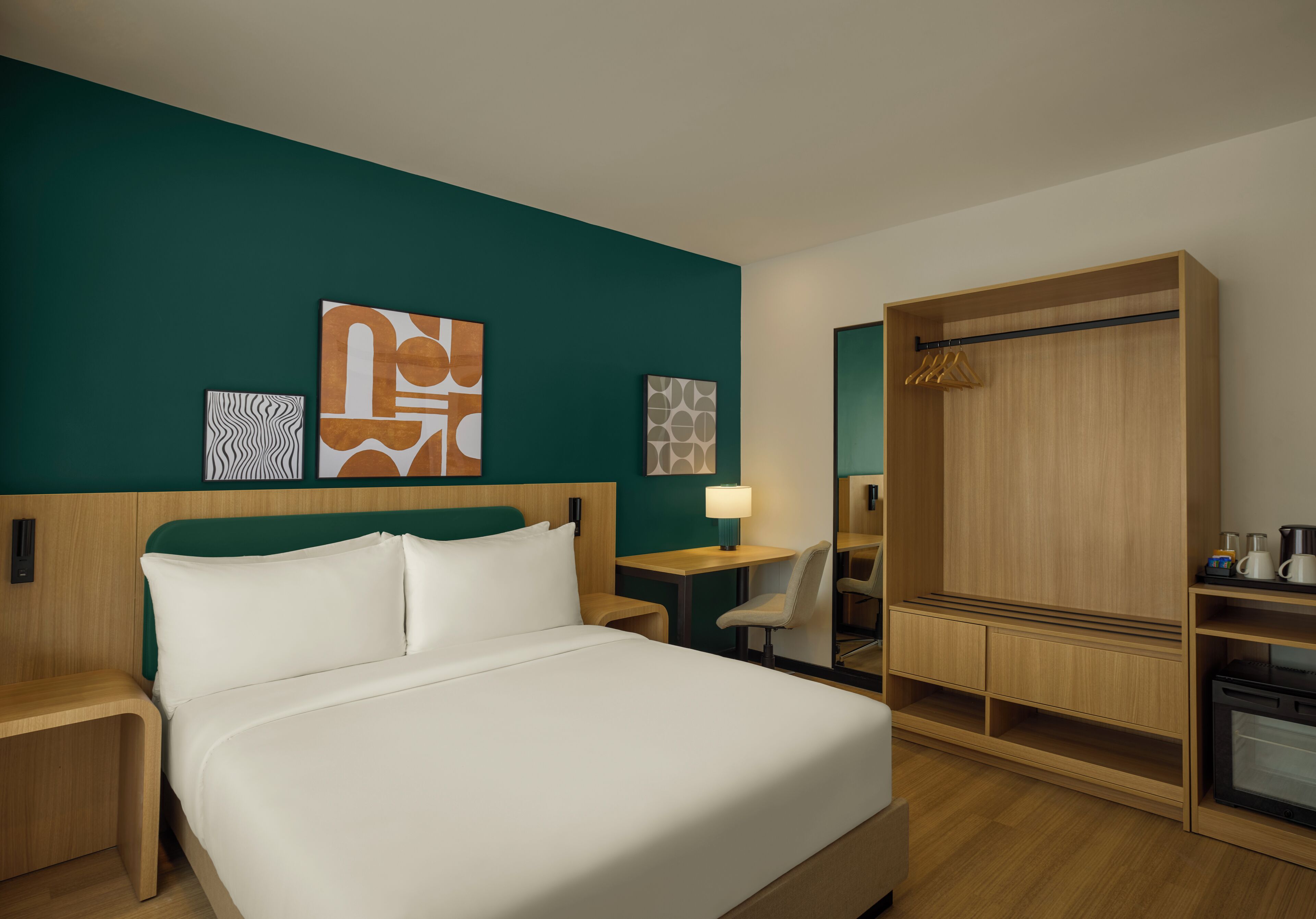 Een hotelkamer met een bed, een bureau, een stoel, een kledingkast en kunst aan de muren.