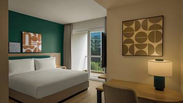 A hotel room with a bed, a desk, a chair, a lamp, and artwork on the walls.