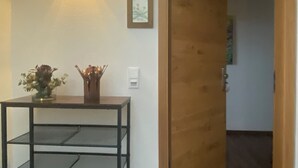Ein Flur mit einer Holztür, einer Wandleuchte, einem gerahmten Bild und einem kleinen Tisch mit einer Vase.