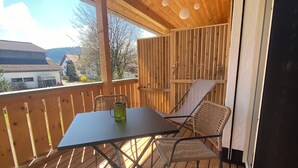 Eine Holzterrasse mit Tisch und Stühlen, Blick auf die Umgebung und eine Holzbalkendecke mit Pendelleuchten.