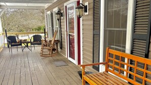 Une terrasse en bois avec un banc et des chaises, un espace couvert avec une porte et une fenêtre dotée de volets.
