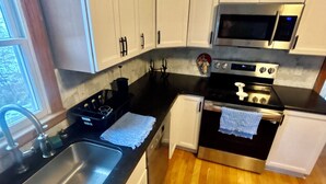 Une cuisine avec des meubles blancs, un évier en acier inoxydable, un four à micro-ondes et une cuisinière.