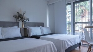 Ett hotellrum med två sängar, en vas med blommor, en stol och en balkong med ett smidesjärnsräcke.