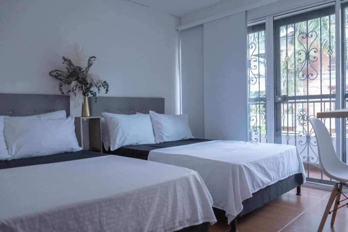 A hotel room with two beds, a vase with flowers, a chair, and a balcony with a wrought iron railing.
