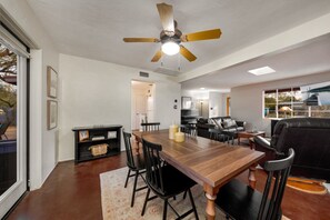 A spacious living room with a wooden dining table, black chairs, a leather sofa, and a ceiling fan. - Cozy 3BR / Fenced Yard & Grill / Near TMC & U of A (Tucson)
