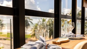 A dining table with a glass, a napkin, and a plate, set against a window with a view of palm trees. - Setai Edition #206 - Waterfront by Carpediem (João Pessoa)