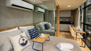 A modern hotel room with a sofa, a small table with a cup, a bed, a dining area, and an air conditioning unit. - Setai Edition #206 - Waterfront by Carpediem (João Pessoa)