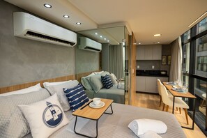 Ein modernes Hotelzimmer mit einer Couch, einem kleinen Tisch mit einer Tasse, einem Bett, einem Essbereich und einer Klimaanlage.