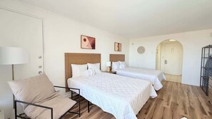 A hotel room with two beds, a chair, a lamp, and artwork on the walls. - Cozy Studio at St. Johns – Steps to Beach (Myrtle Beach)