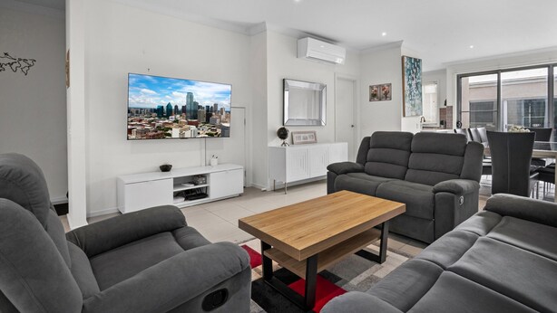 A modern living room with grey sofas, a wooden coffee table, a flat-screen TV, and a cityscape painting on the wall. - Spacious 3-bed Townhouse in Coburg (Melbourne)