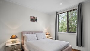 A bedroom with a bed, bedside tables, a nightstand, a window with curtains, and a wall-mounted picture. - Spacious 3-bed Townhouse in Coburg (Melbourne)