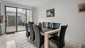 A dining area with a glass table and black chairs, a vase with flowers, and a painting on the wall. - Spacious 3-bed Townhouse in Coburg (Melbourne)