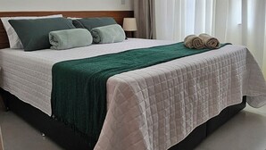 A neatly made bed with a green and white quilt, a wooden headboard, and a brown doormat in a hotel room. - Apê Maré Blue - Seu Paraíso à beira-mar! (ILHEUS)